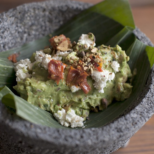 Guacamole with garnishes in a stone bowl lined with plantain leaves