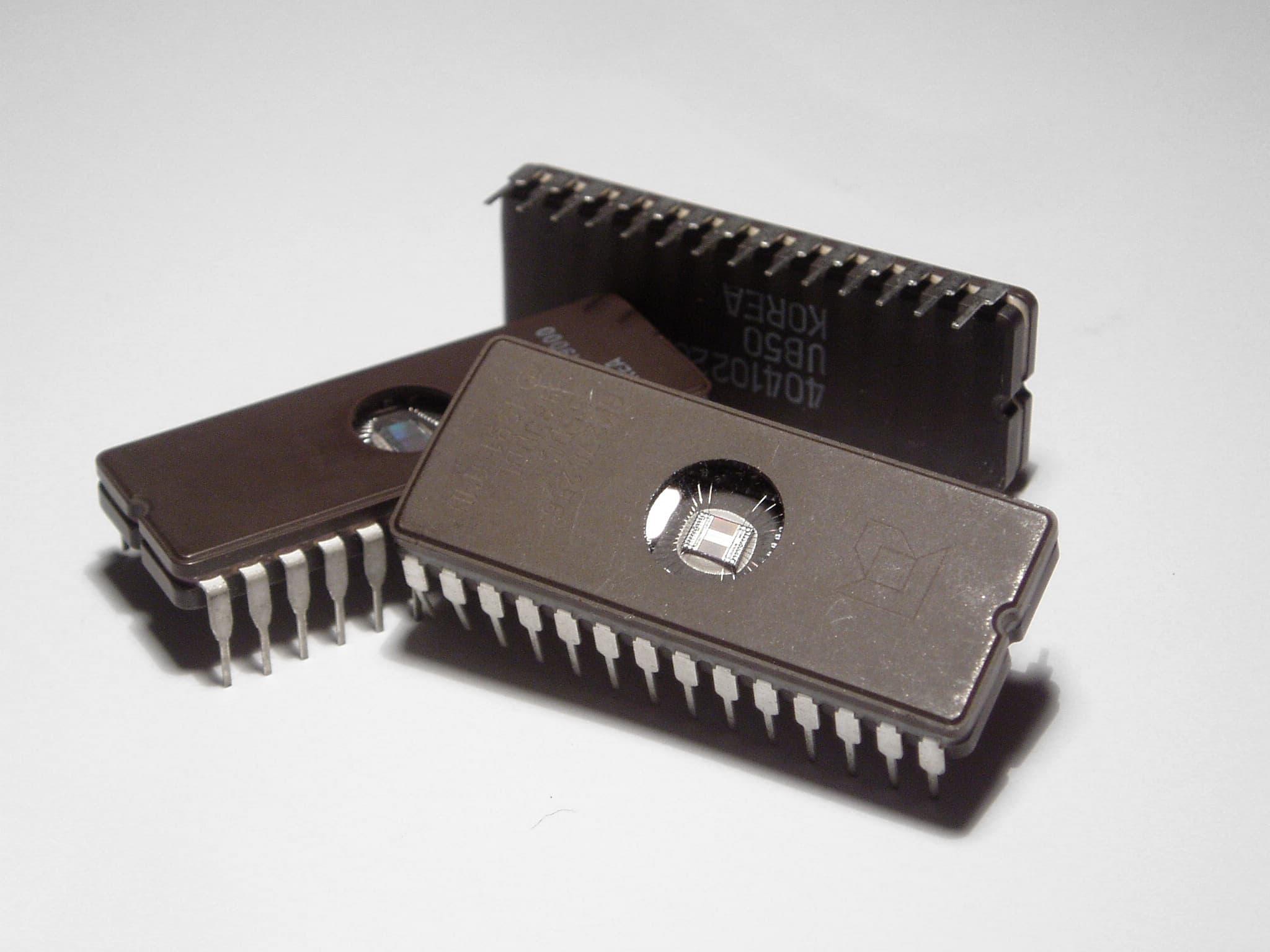 Close up product shot of three EPROM chips, showing the tiny integrated circuit through a hole in the top